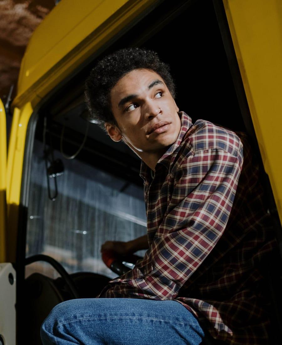 Truck driver in a plaid shirt sitting in the cab of a yellow truck